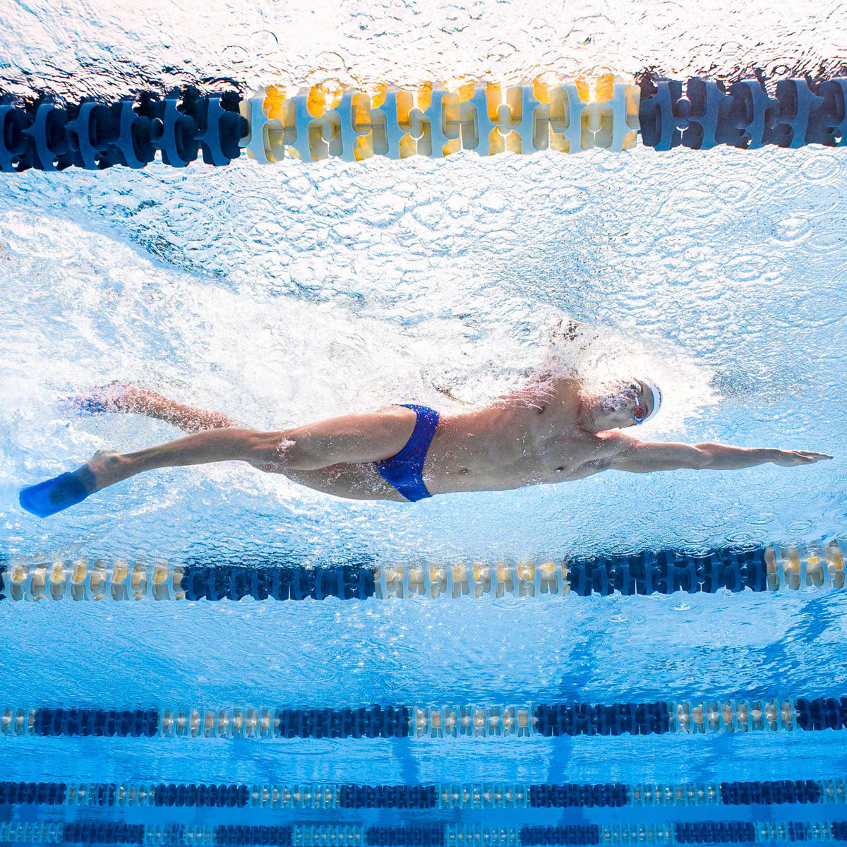 Wide underwater view of a swimmer in a blue brief doing free style stroke while wearing blue FINIS SlipFin Pro swim fins.