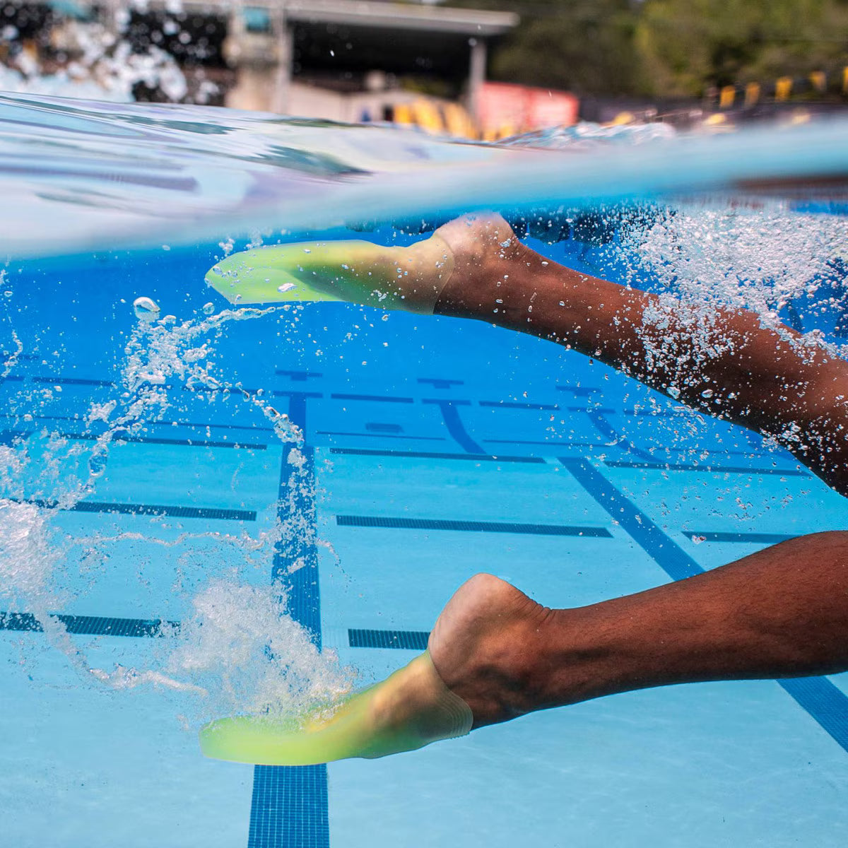 Underwater side profile of a swimmer’s legs kicking with translucent volt green FINIS SlipFin Pro swim fins, creating bubbles.
