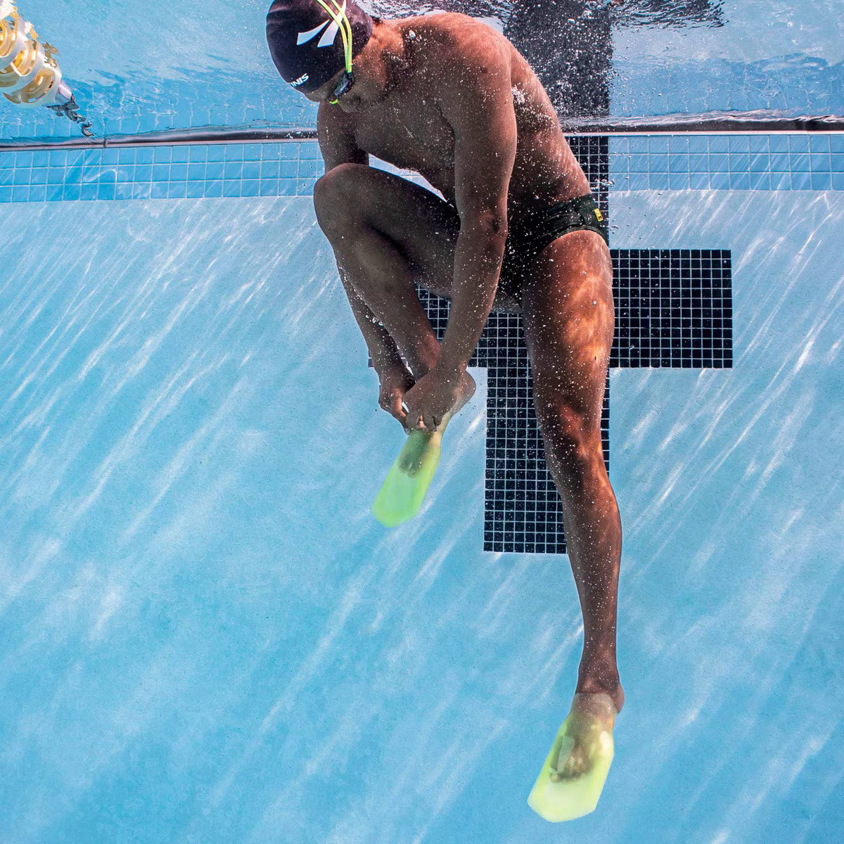 Underwater view of a male swimmer adjusting a translucent volt green FINIS SlipFin Pro swim fin on his foot while submerged.